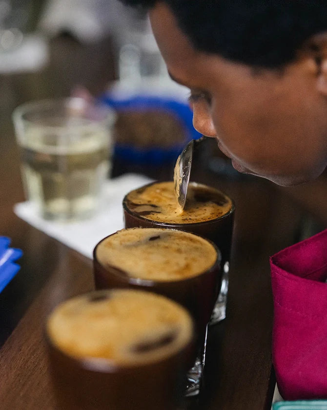 A person tasting coffee from small cups with a spoon on a wooden table.