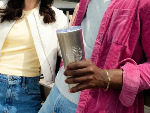 Two people standing together, one holding a Starbucks Pearlized Cold Cup, another wearing a two-toned Starbucks Cap.