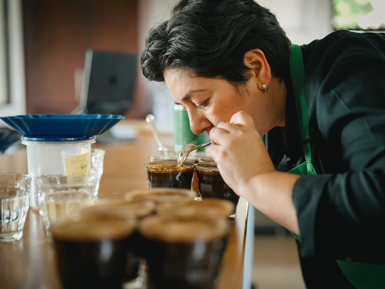 Person tasting coffee in a bar setting with various coffee cups and a blue funnel.
