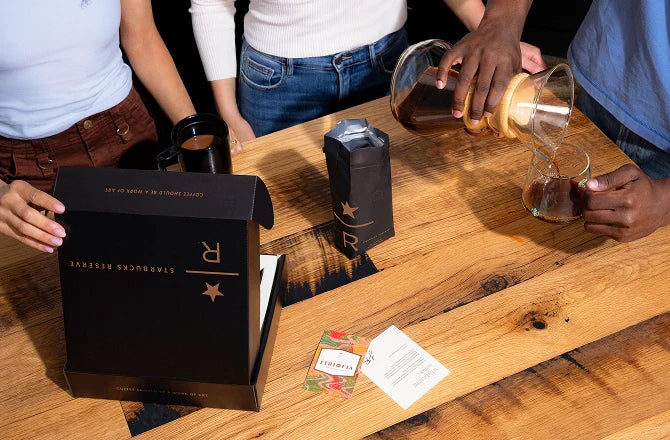 People around a wooden table with a box labeled 'R' and a person pouring liquid into a glass.