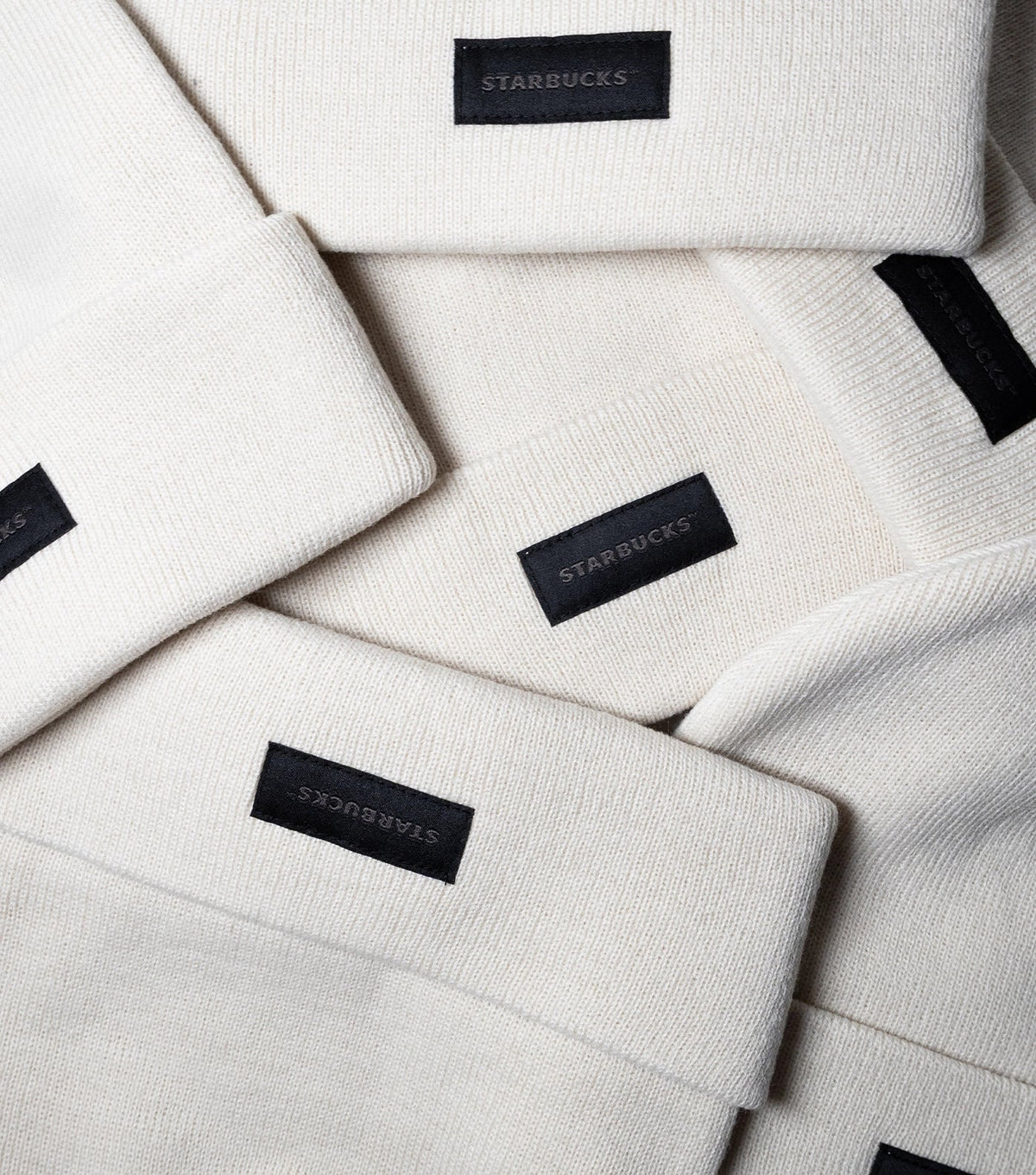 A stack of natural beige Starbucks Knit Beanies with a black Starbucks tag at the front.