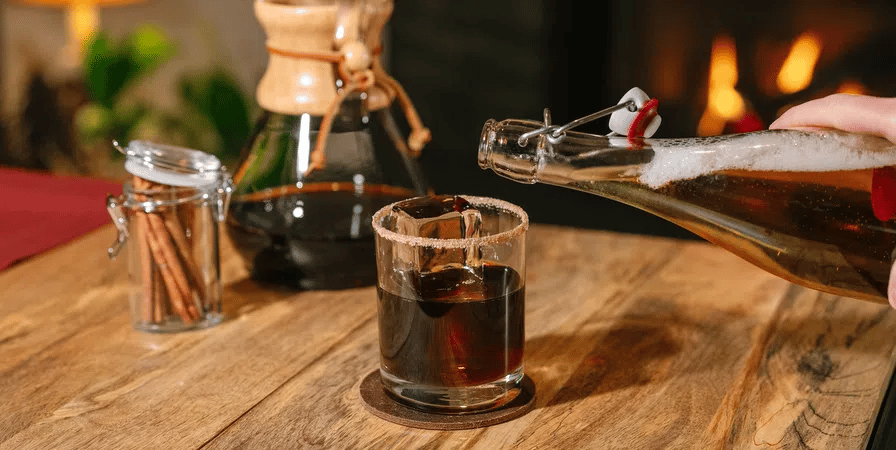 Glass of Iced Coffee Apple Pie on a wooden surface, with a coffee maker in the background.