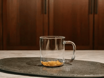 Clear glass mug with a small amount of sand on a dark round coaster against a wooden background