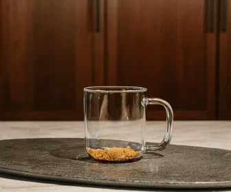 Clear glass mug with a small amount of sand on a dark surface with a wooden background
