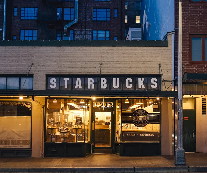 Starbucks store exterior at night with illuminated sign and window display.