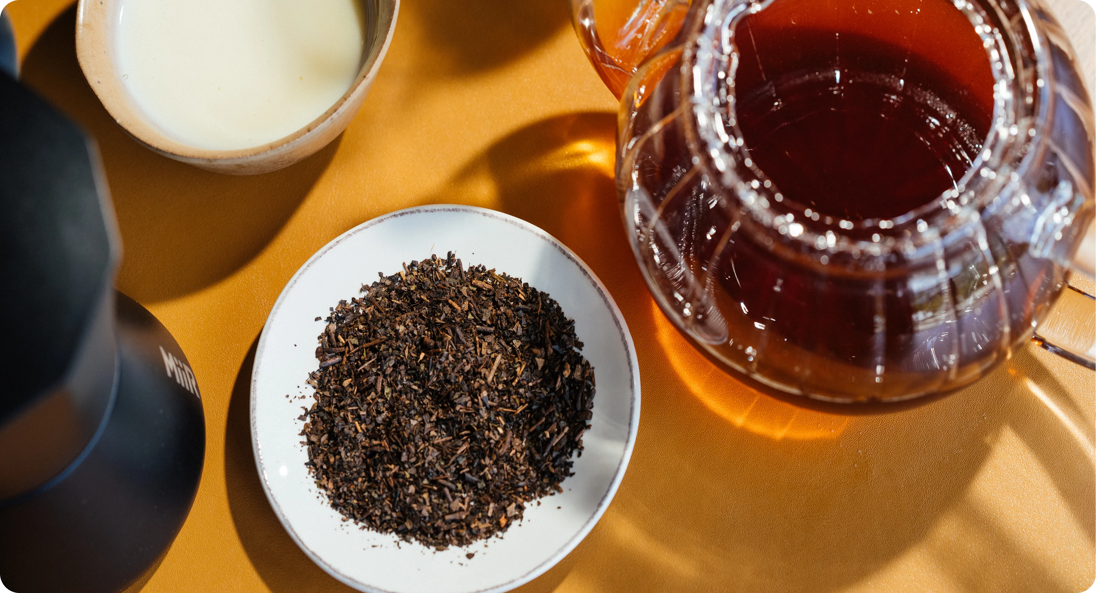 Tea-making setup with a teapot, loose tea leaves, and a bowl of tea on a wooden surface.