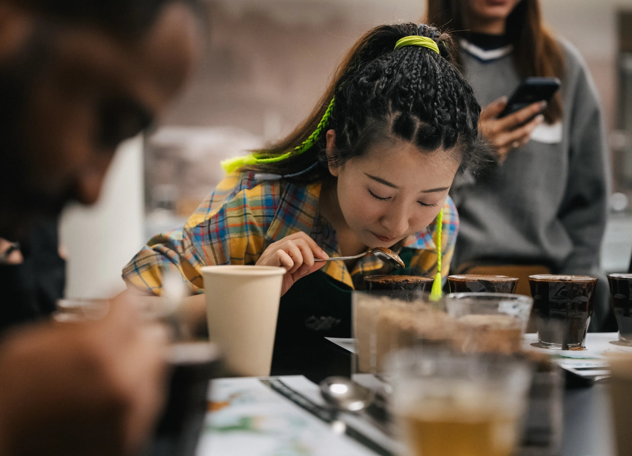 Person eating at a table with various drinks and people in the background