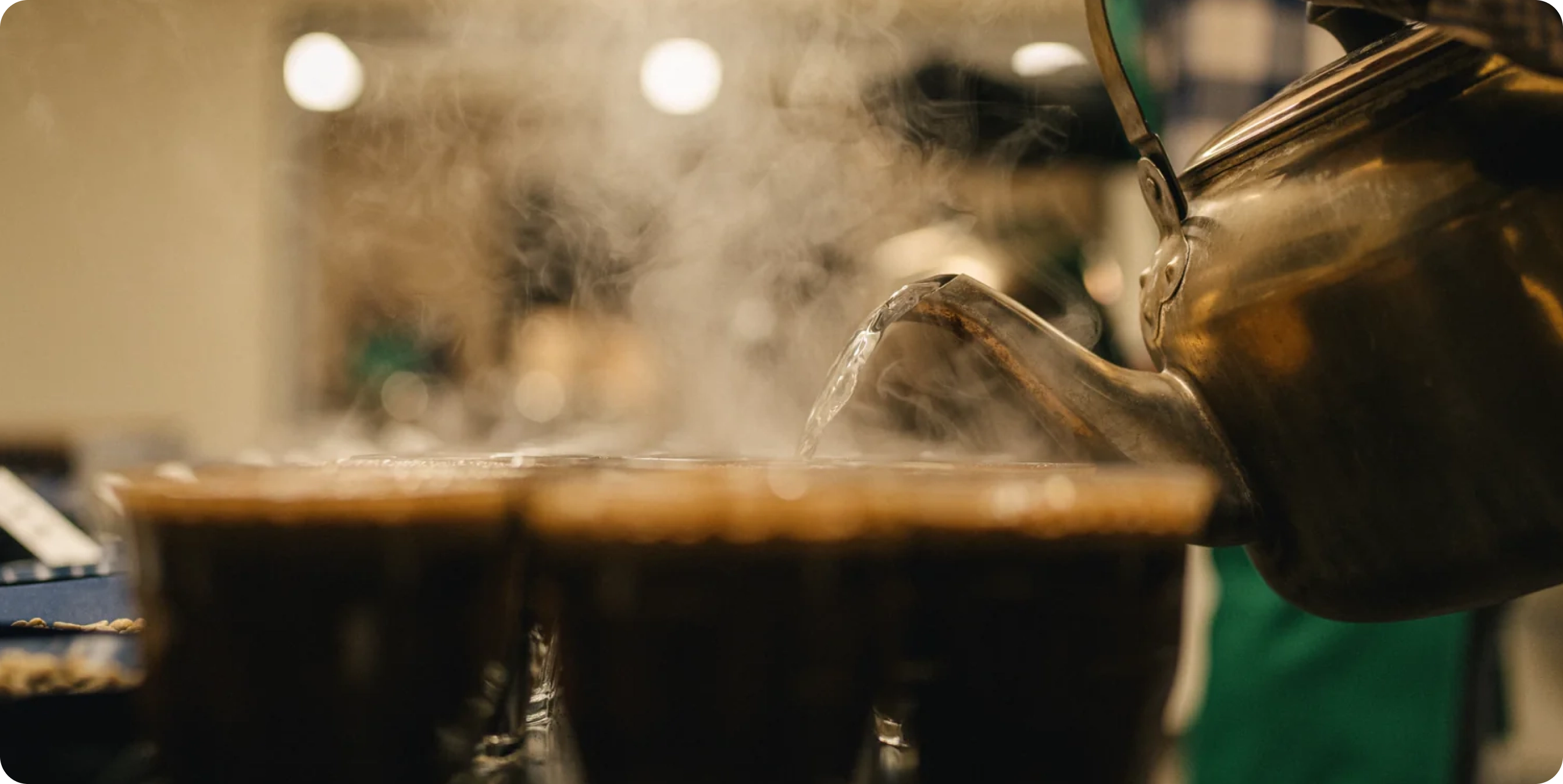 Steaming hot liquid being poured from a teapot into a cup with a blurred background
