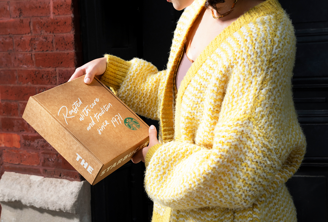 Person holding a Starbucks coffee box against a brick wall.