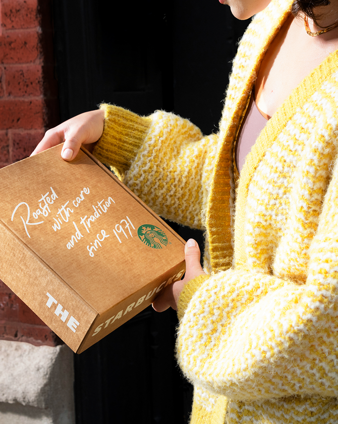 Person holding a Starbucks coffee box with a yellow sweater