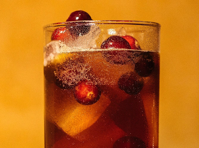 Glass of sparkling berry drink with ice cubes on a warm yellow background