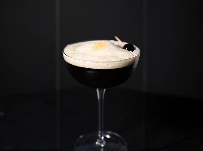 Close-up of a glass of cold brew lemon sour, with a layer of froth and skewer on top.