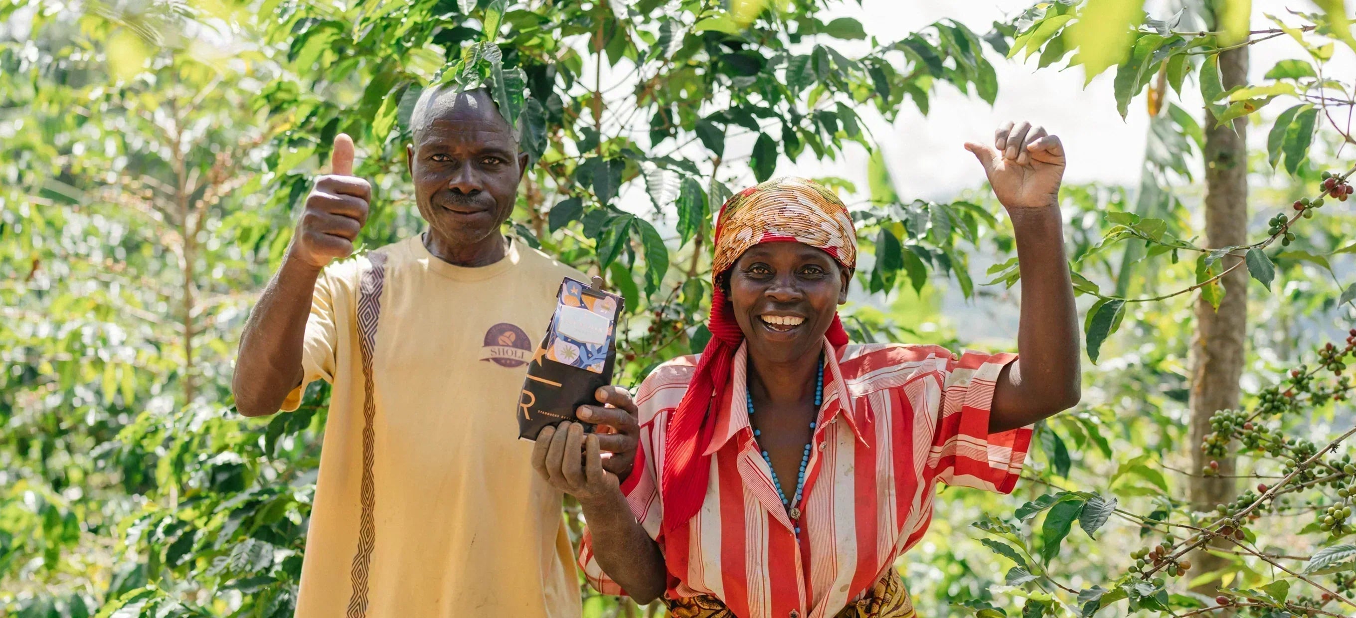 A smiling man and woman stand among coffee plants and give a thumbs up, holding a bag of Starbucks Reserve coffee.