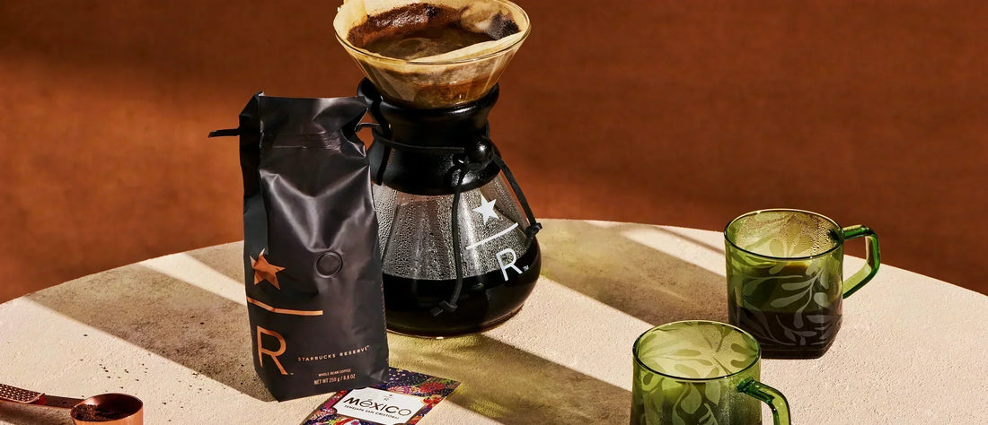 A Starbucks Reserve pour-over brewer and coffee bag on a table with two green glass mugs.