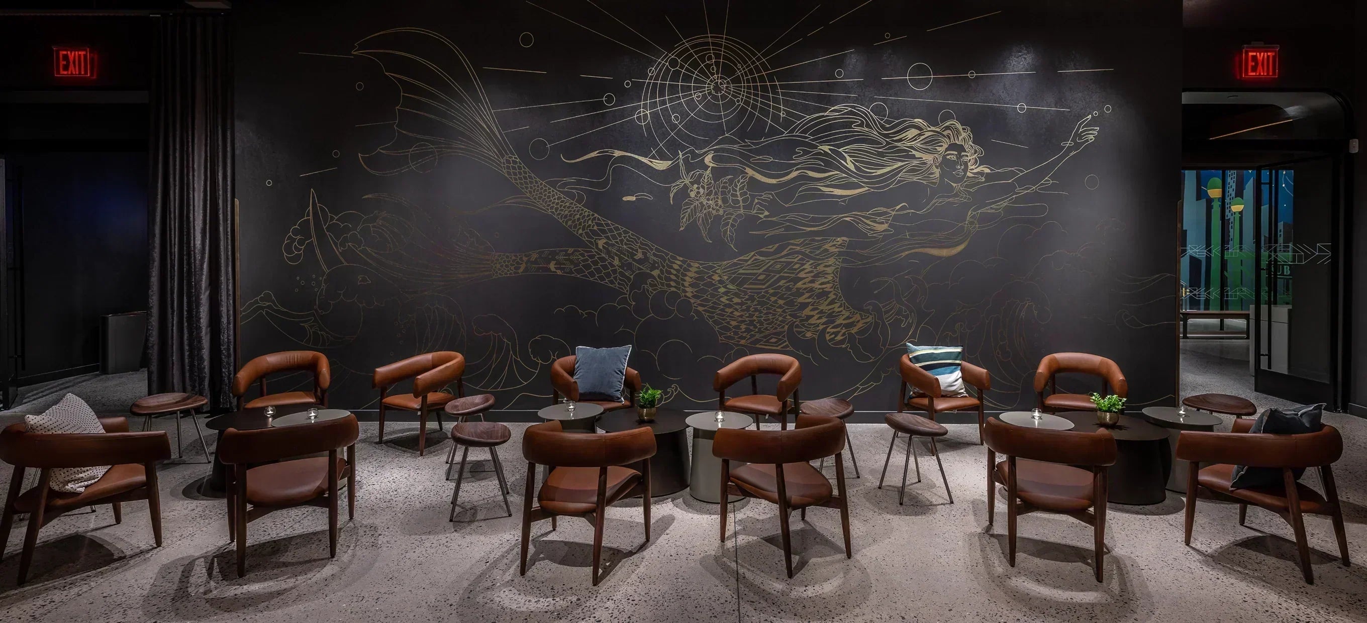 A cafe seating area with leather chairs in front of a large wall mural of a golden Starbucks siren.