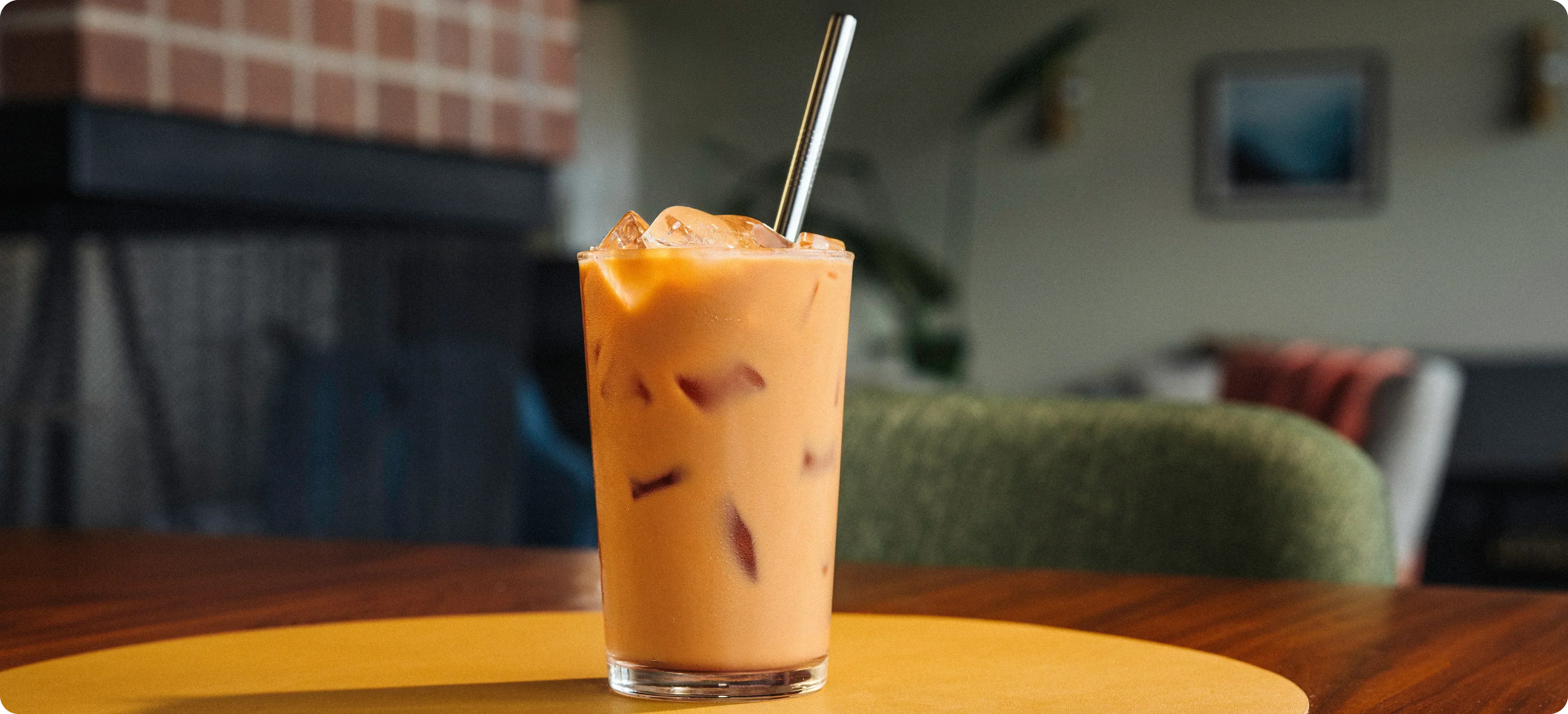 Iced coffee with a straw in a glass on a wooden table, blurred indoor background