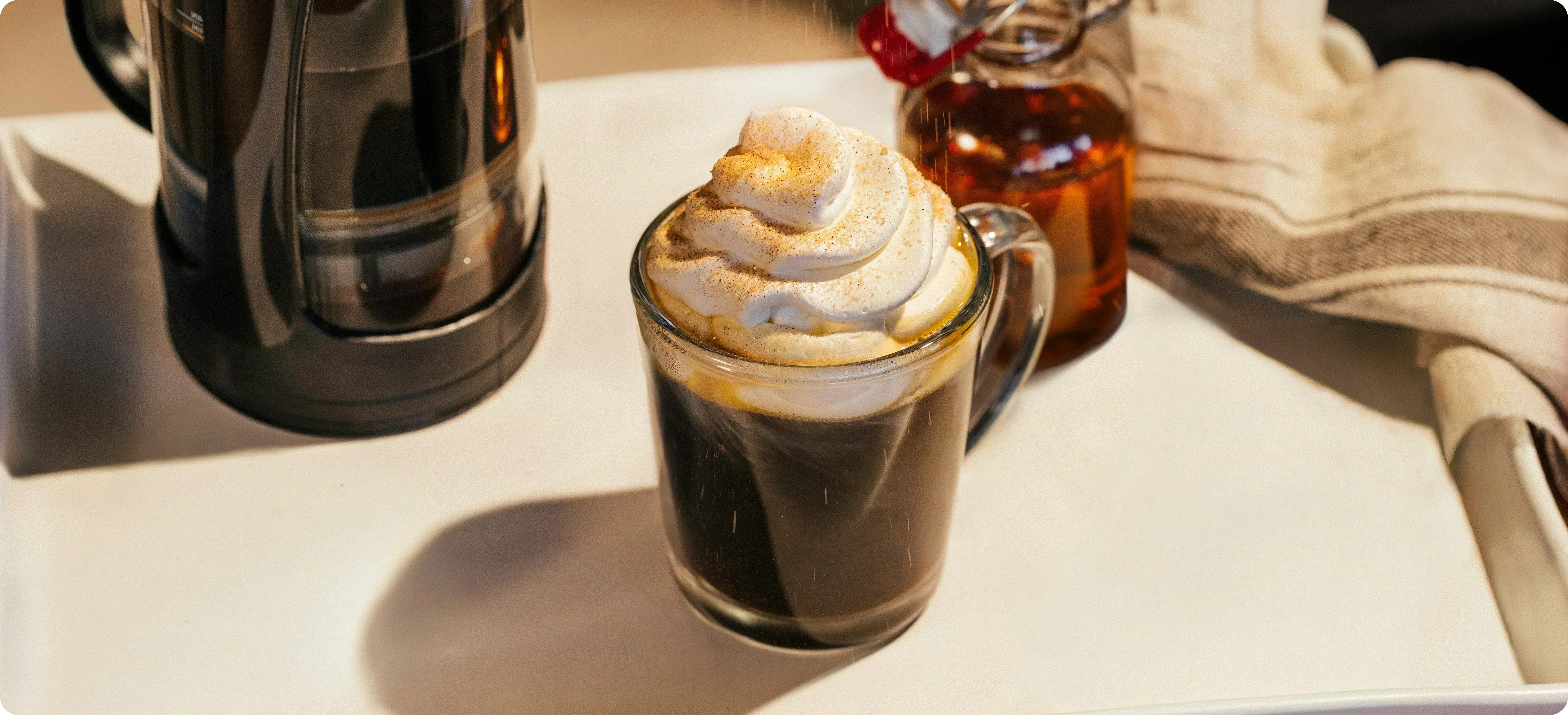 Glass of coffee with whipped cream and a bottle of syrup on a table
