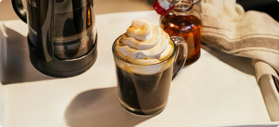 Glass of coffee with whipped cream and a bottle of syrup on a table
