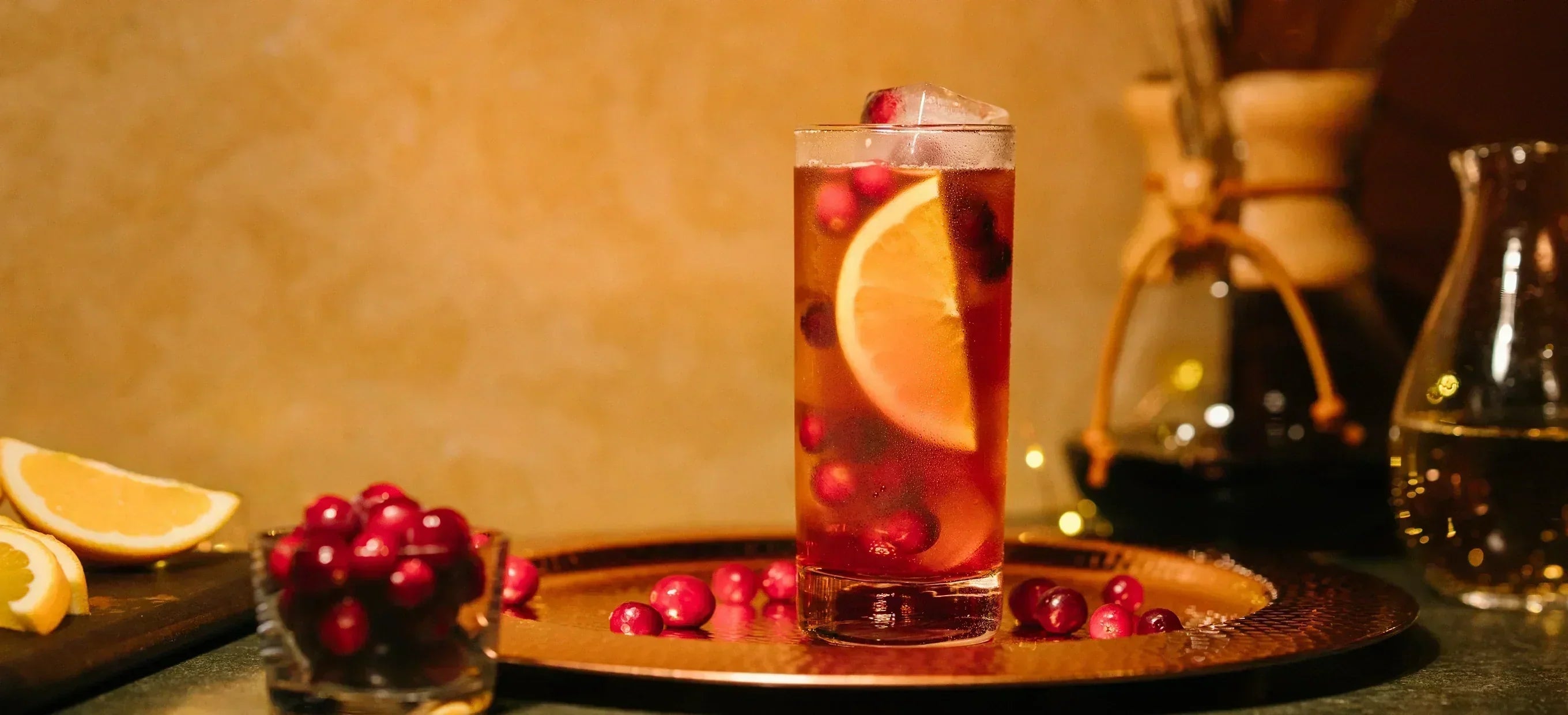 Glass of iced tea with orange slices and cranberries on a wooden tray with a blurred background