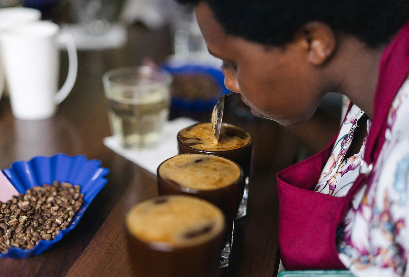 A person tasting coffee from small cups with a spoon on a wooden table.