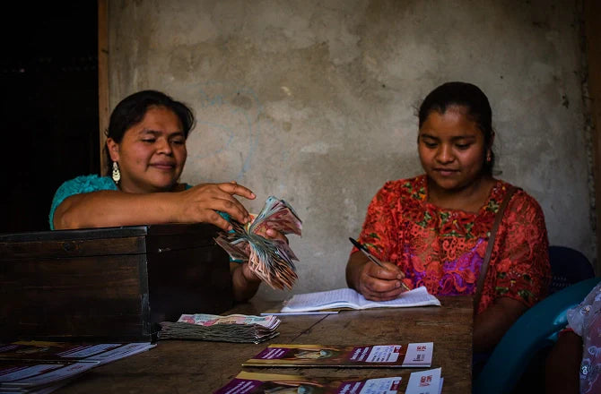 Two women sitting at a table with money and documents in a dimly lit room.