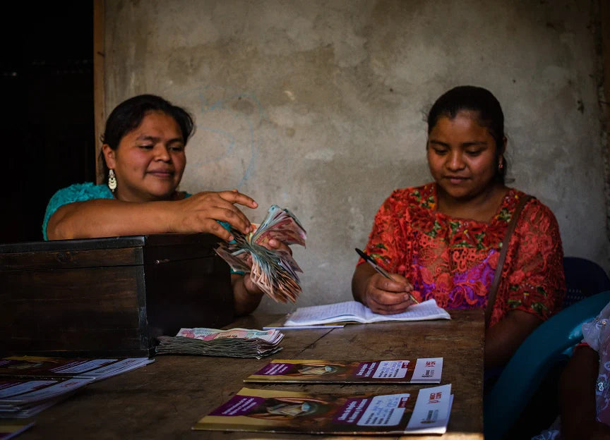 Two women sitting at a table with money and documents in a dimly lit room.