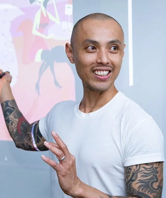 The artist, Marcos Chin pointing at a colorful display board in an office setting.