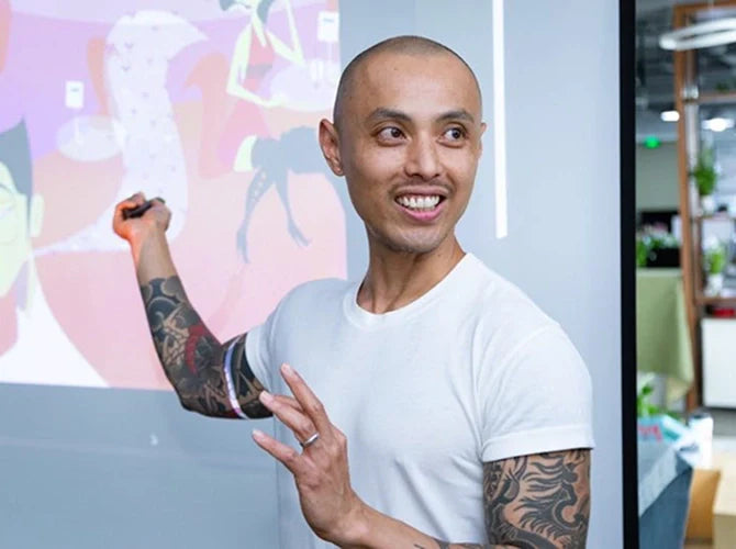 The artist, Marcos Chin pointing at a colorful display board in an office setting.