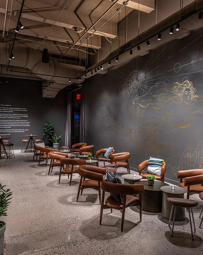 Modern interior of the Starbucks Reserve Empire State Building store, with brown chairs and tables against decorative wall art by Marcos Chin.