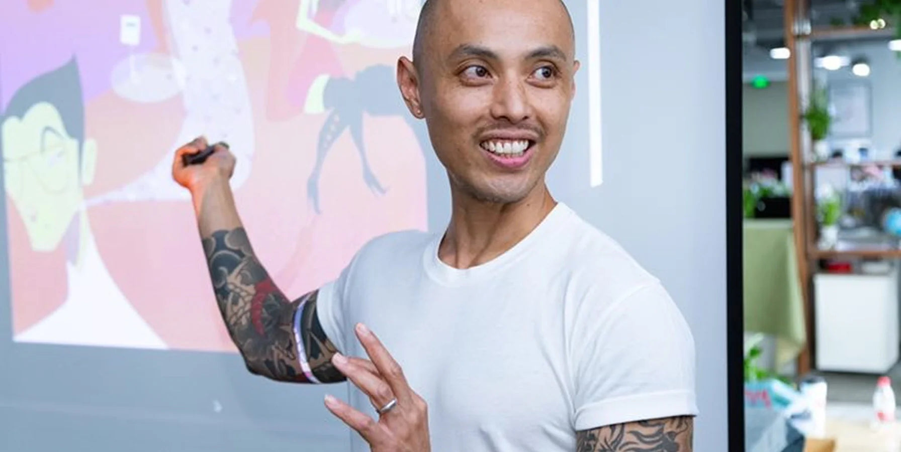 The artist, Marcos Chin pointing at a colorful display board in an office setting.