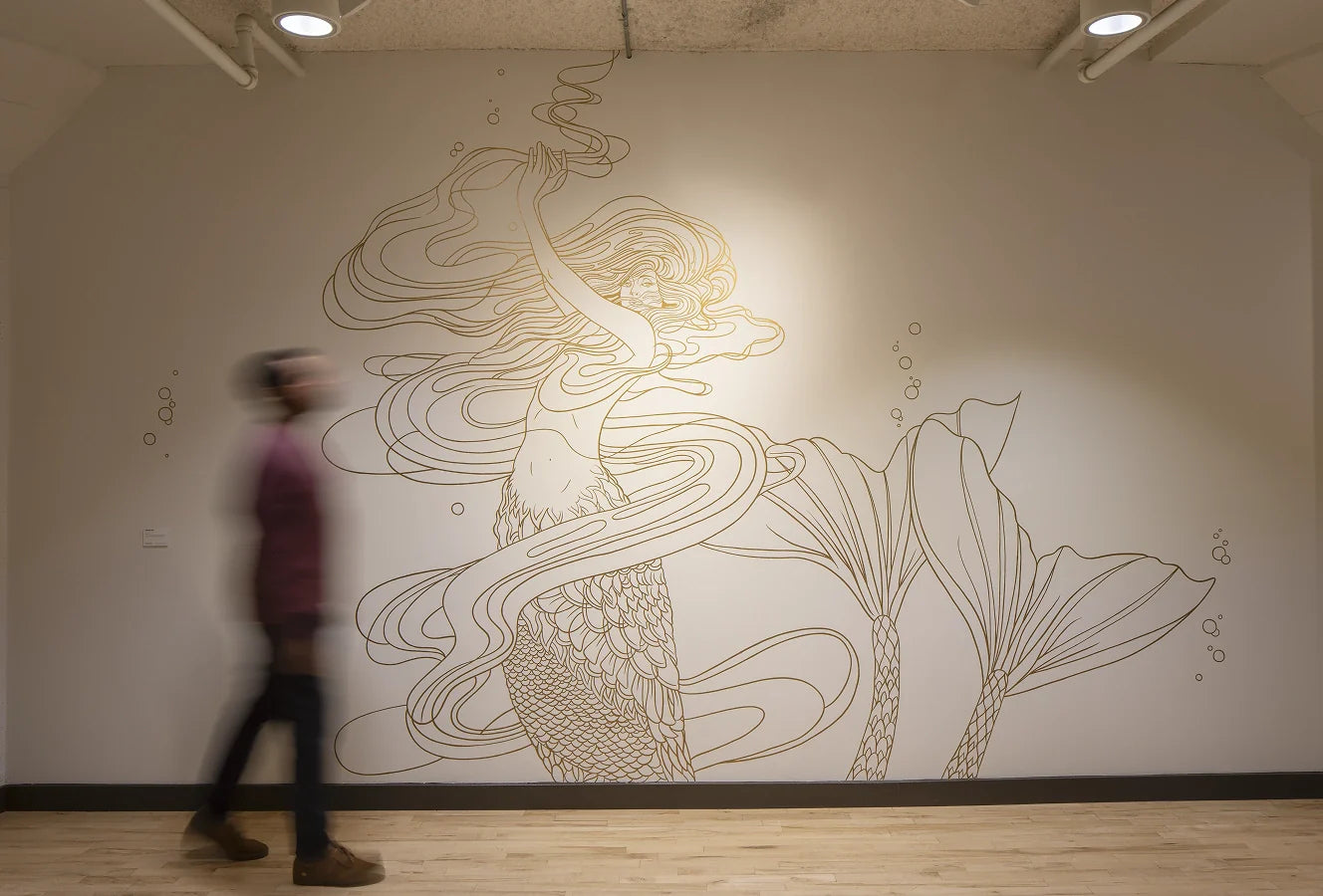 A person walking past a wall with a large, detailed Art Deco illustration artwork by Marcos Chin.
