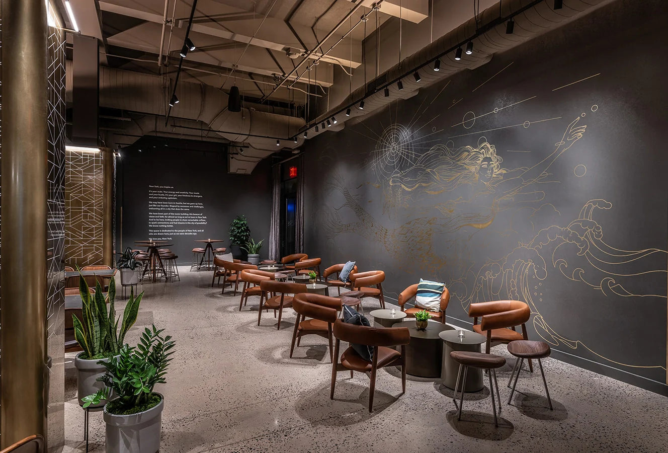 Modern interior of the Starbucks Reserve Empire State Building store, with brown chairs and tables against decorative wall art by Marcos Chin.