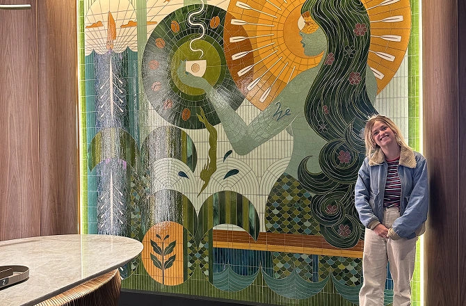The artist, Becca Fuhrman, standing in front of her floor-to-ceiling mosaic artwork.