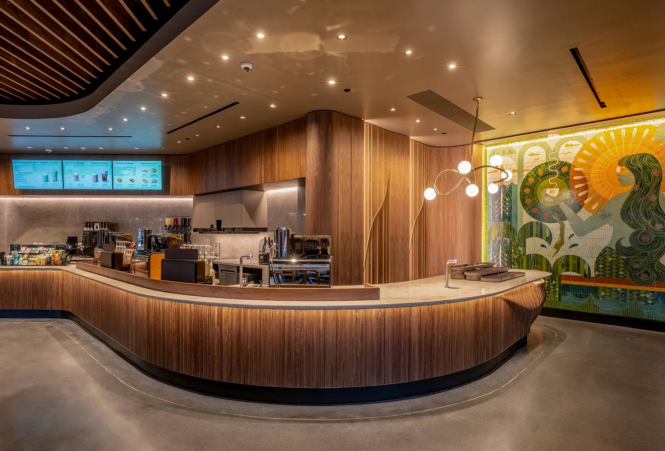 Interior of a Starbucks coffeehouse, with wooden textures, marble countertops and decorative mosaic wall art by Becca Fuhrman.