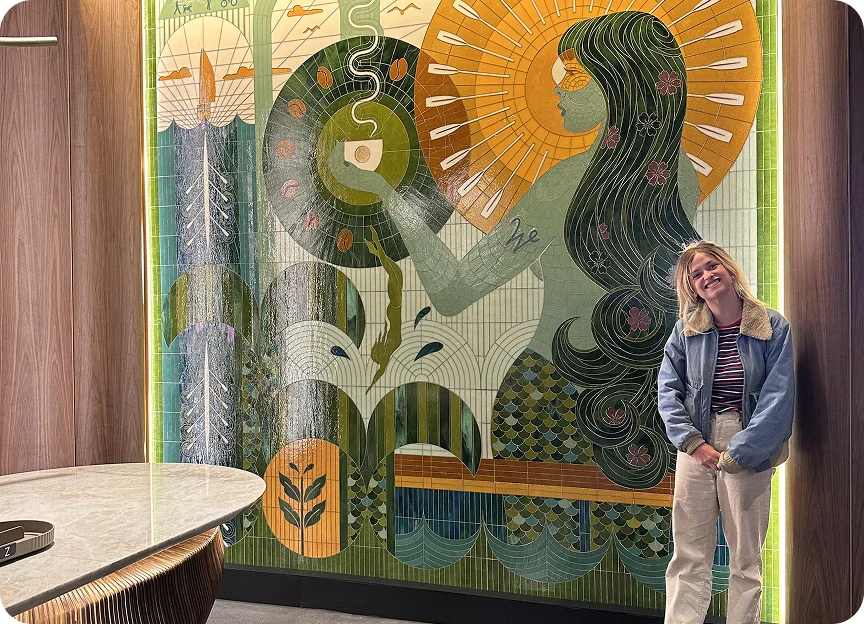 The artist, Becca Fuhrman, standing in front of her floor-to-ceiling mosaic artwork.