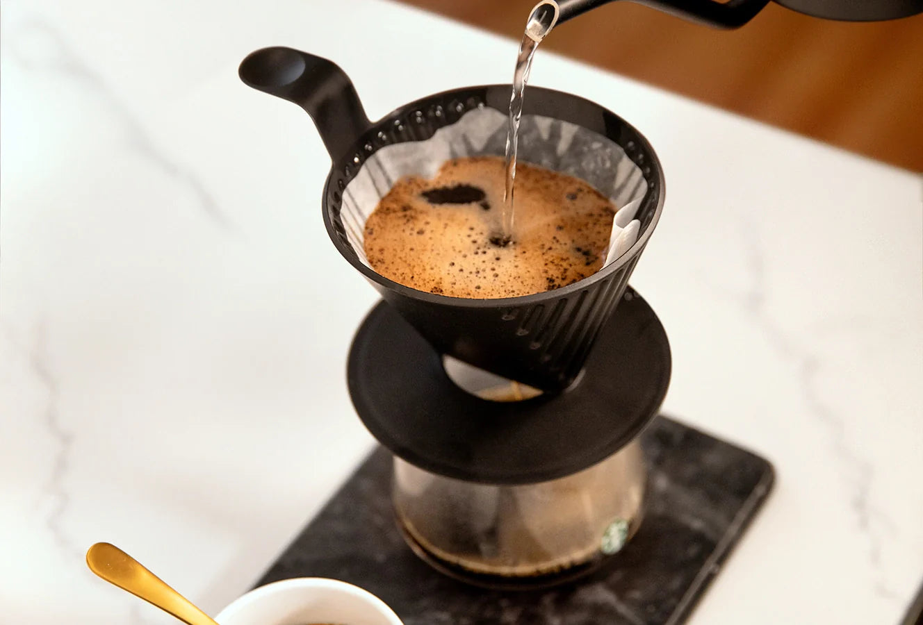 Water being poured into a filter basket, with coffee brewing through a Starbucks Plastic Pour Over.