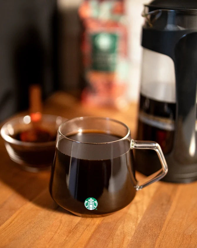 A Starbucks Glass Mug filled with coffee on a wooden surface with a blurred background.