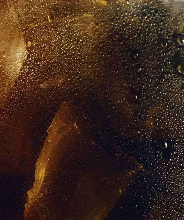 Video showing a close-up shot of a coffee drink with ice cubes, water condensation and milk. More milk is being poured into the liquid, slowly expanding until it mixes with the rest of the liquid.