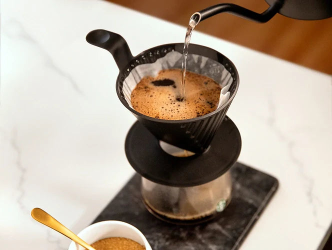 Water being poured into a filter basket, with coffee brewing through a Starbucks Plastic Pour Over.