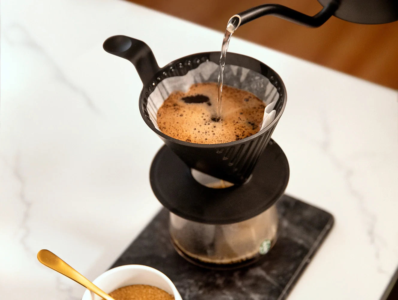 Water being poured into a filter basket, with coffee brewing through a Starbucks Plastic Pour Over.