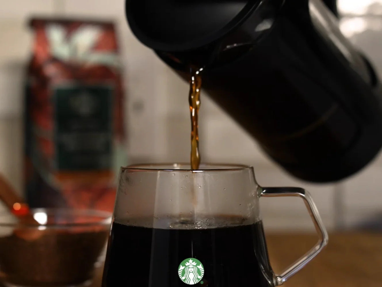 Coffee being poured into a Starbucks Glass Mug with a blurred background.