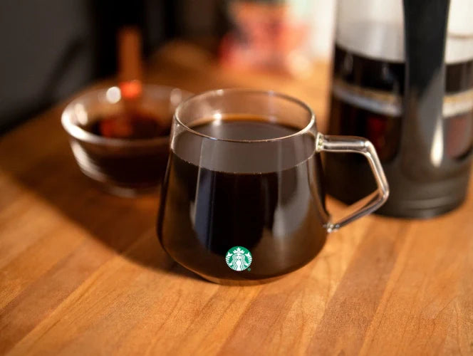 Starbucks Glass Mug with coffee on a wooden table with a blurred background.