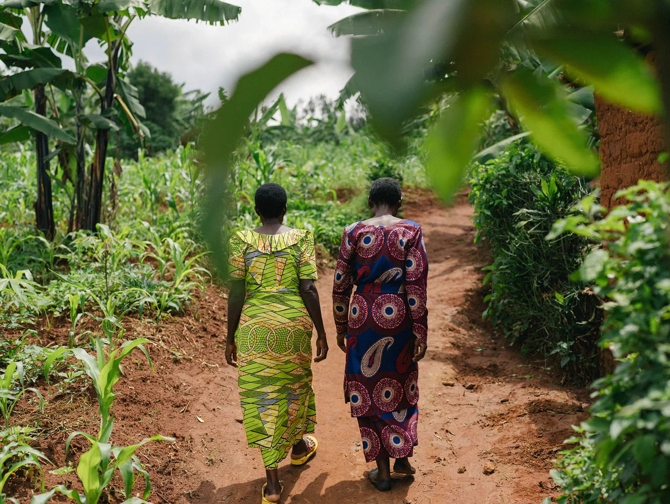 Two women walking along a dirt path in a lush green garden.