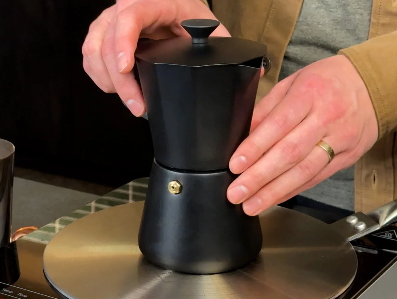 Coffee expert, Lincoln, placing a black Miir Moka Pot Espresso Maker on top of a flat metal induction adapter plate.