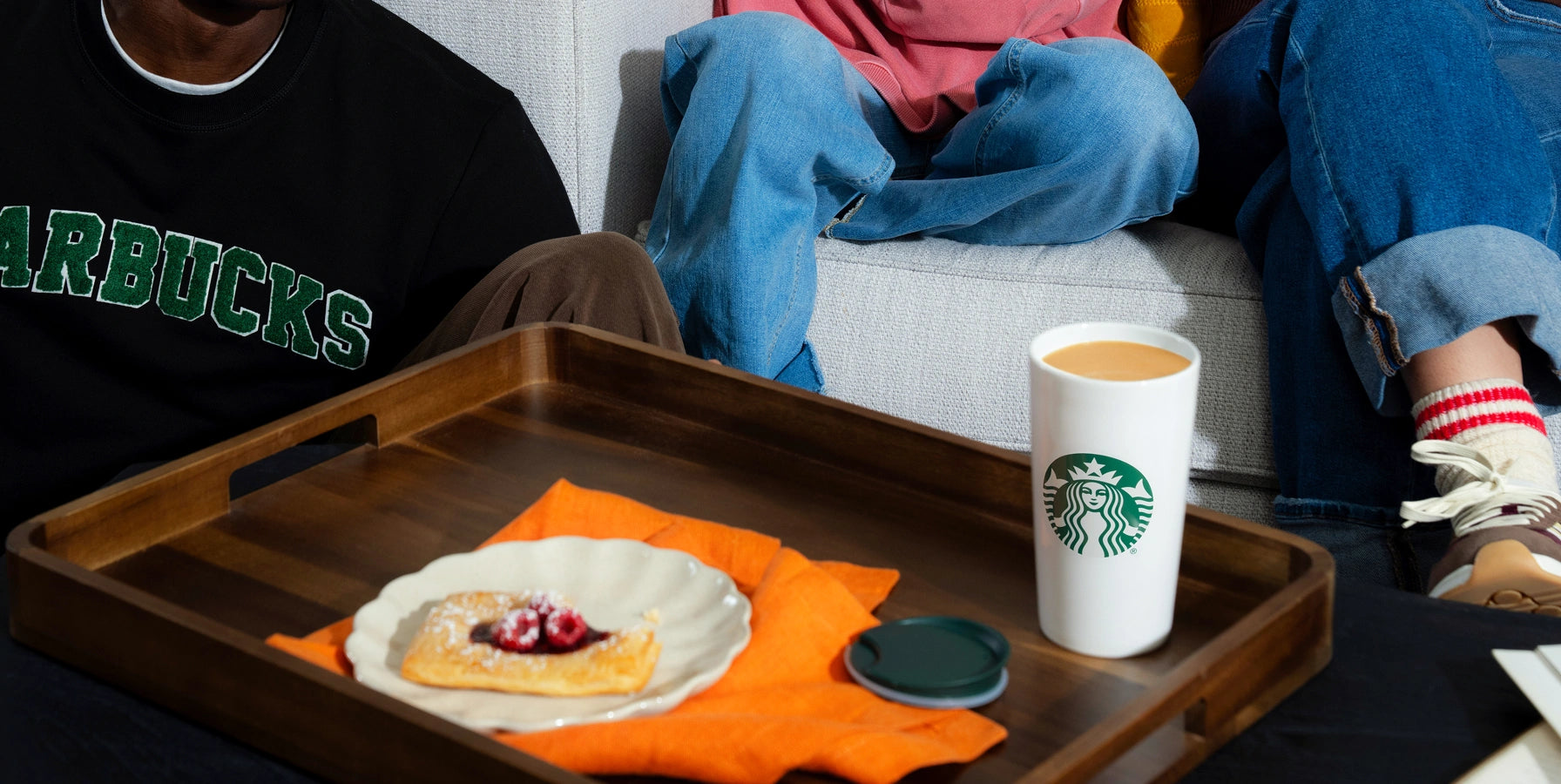 Starbucks cup on a tray with food, person sitting on a couch in the background