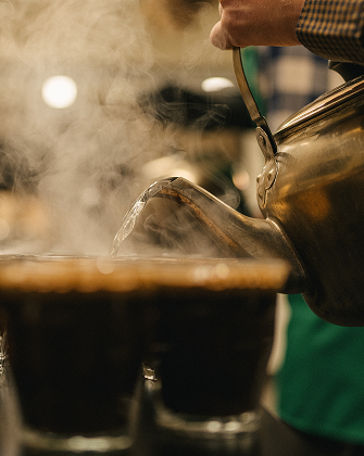Person pouring steaming hot liquid from a teapot into two cups.