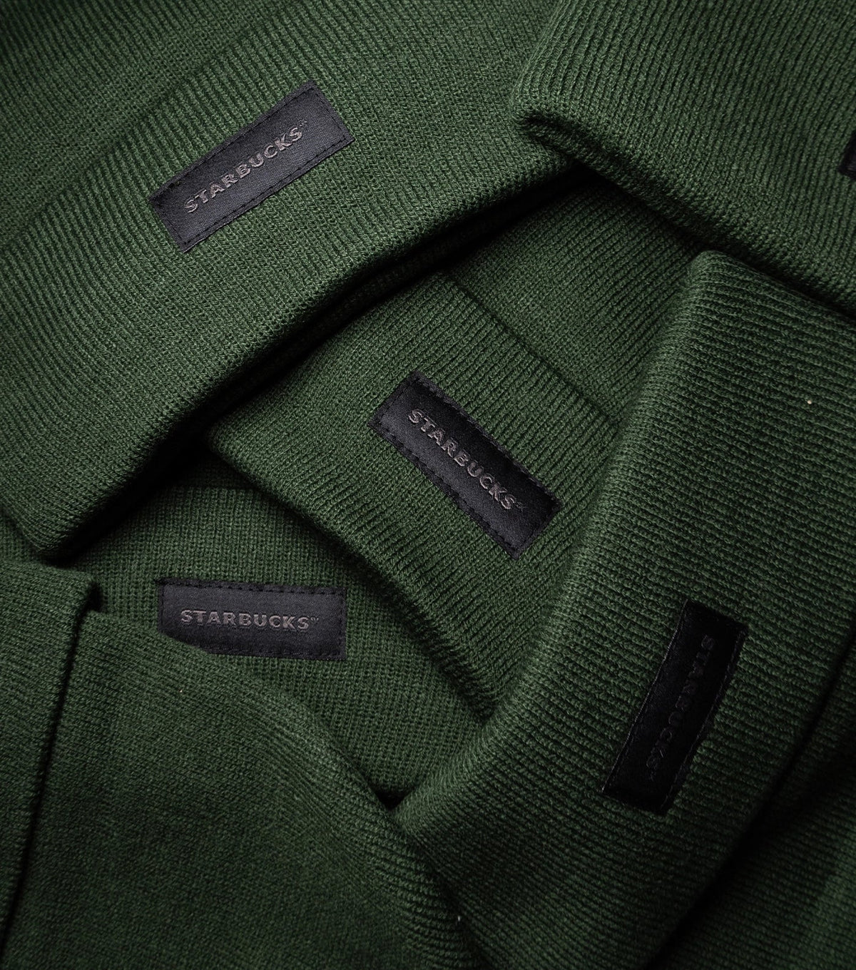 A stack of green Starbucks Knit Beanies with a black Starbucks label at the front.