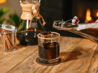 Glass of Iced Coffee Apple Pie on a wooden surface, with a coffee maker in the background.