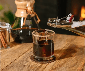 Glass of Iced Coffee Apple Pie on a wooden surface, with a coffee maker in the background.