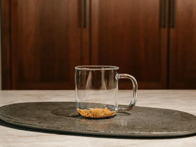 Clear glass mug with brown sugar on a dark gray mat against a wooden background.